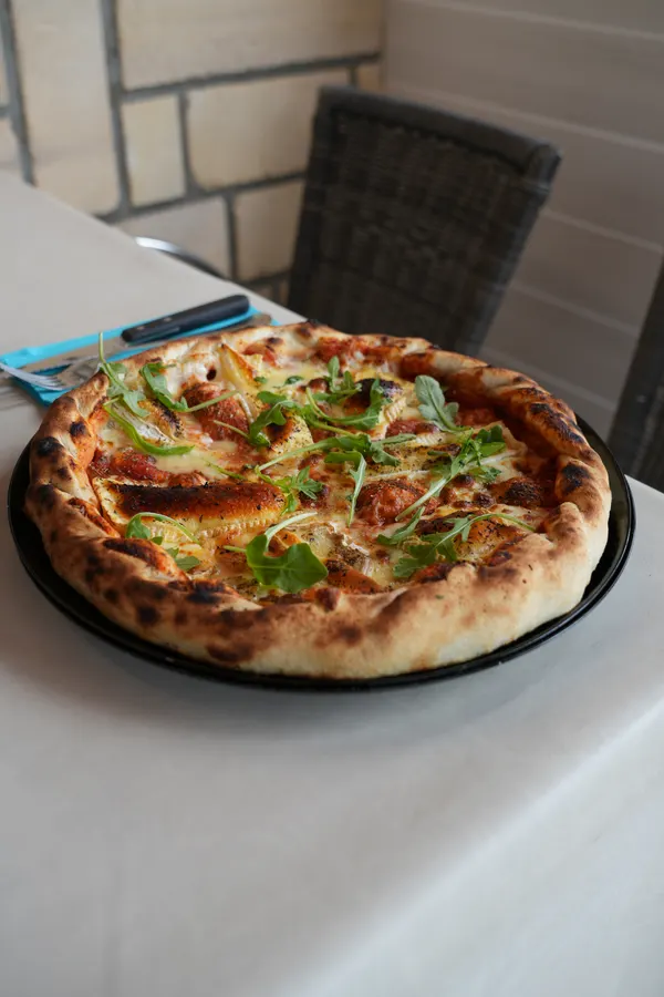Pizza maison généreusement garnie servie sur une table du Novoli